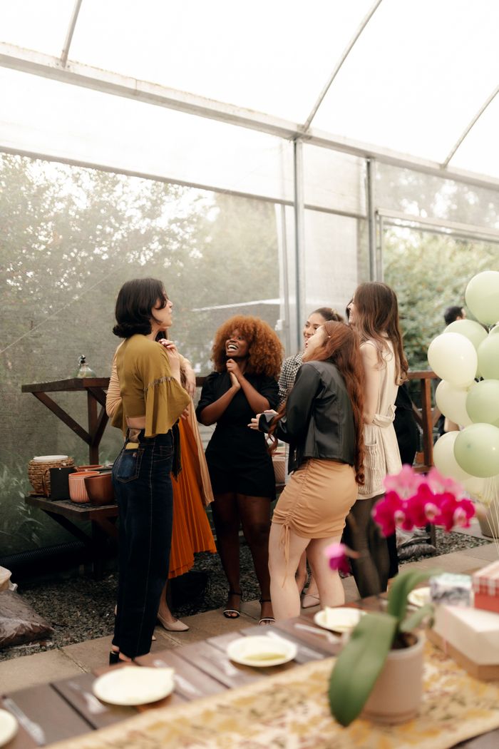 A diverse group of women enjoying a casual indoor gathering with balloons and flowers.